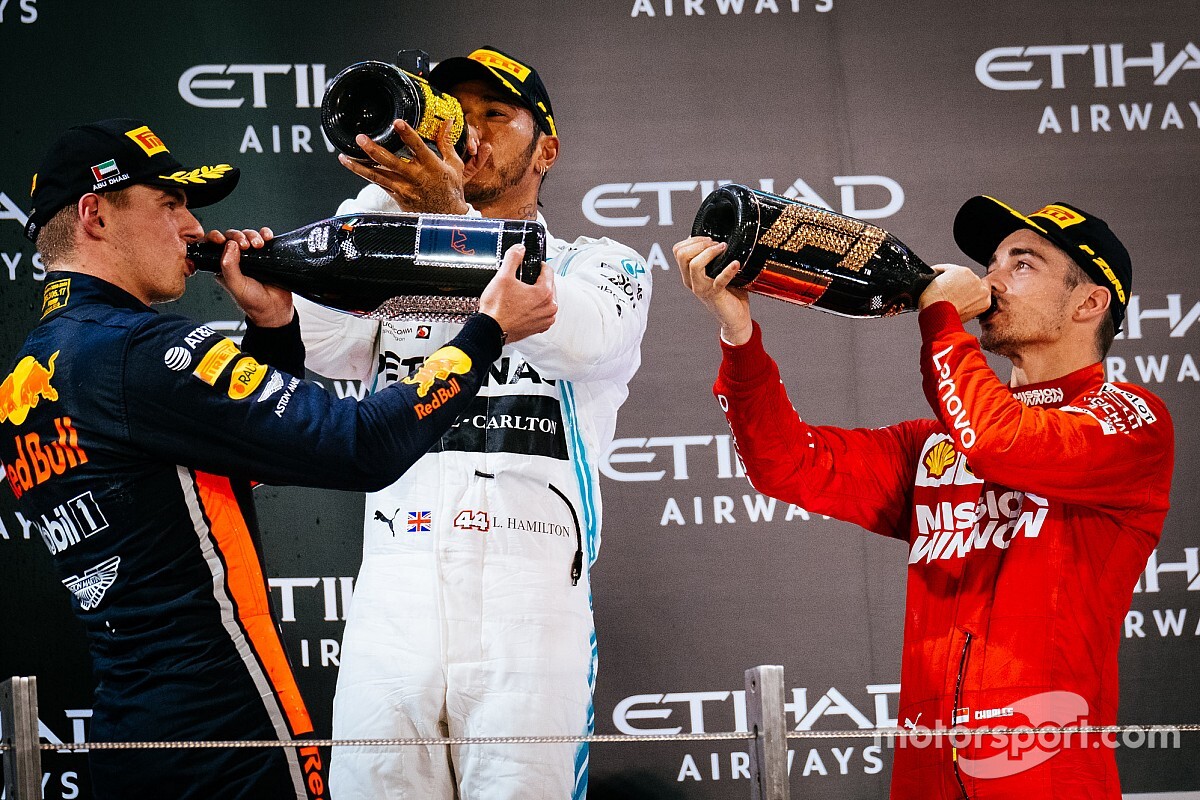 3 famous f1 drivers standing up and drinking from beddazled bottles